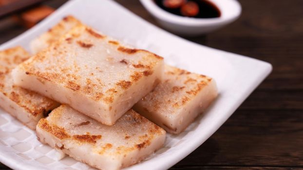 Delicious turnip cake, Chinese traditional local dish radish cake in restaurant with soy sauce and chopsticks, close up, copy space.