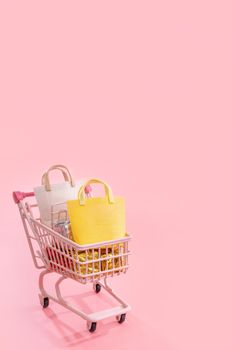 Annual sale shopping season concept - mini pink shop cart trolley full of paper bag gift isolated on pale pink background, blank copy space, close up