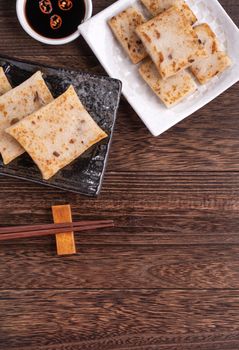 Delicious turnip cake, Chinese traditional local radish cake in restaurant with soy sauce and chopsticks, close up, copy space, top view, flat lay.