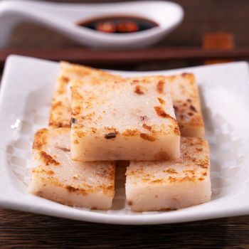 Delicious turnip cake, Chinese traditional local dish radish cake in restaurant with soy sauce and chopsticks, close up, copy space.