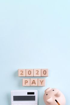 2020 goal, finance plan abstract design concept, wood blocks on blue table background with piggy bank and calculator, top view, flat lay, copy space.