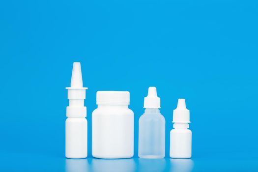 Medication pills, ear drops, eye drops and nose spray against blue background with copy space. Concept of health care and medications for treating cold-related diseases and flue