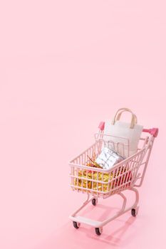 Annual sale shopping season concept - mini pink shop cart trolley full of paper bag gift isolated on pale pink background, blank copy space, close up