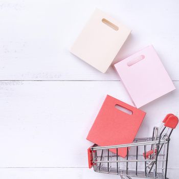 Abstract design element,annual sale,shopping season concept,mini cart with colorful paper bag on white wooden table background,top view,flat lay