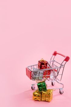 Annual sale, Christmas shopping season concept - mini red shop cart trolley full of gift box isolated on pale pink background, copy space, close up