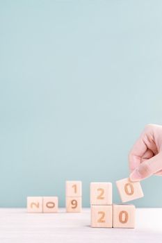 Abstract 2020 & 2019 New year countdown design concept - woman holding wood blocks cubes on wooden table and green background, close up, copy space.