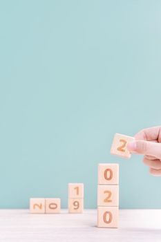 Abstract 2020 & 2019 New year countdown design concept - woman holding wood blocks cubes on wooden table and green background, close up, copy space.