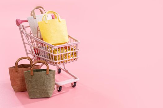 Annual sale shopping season concept - mini pink shop cart trolley full of paper bag gift isolated on pale pink background, blank copy space, close up
