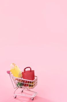 Annual sale shopping season concept - mini pink shop cart trolley full of paper bag gift isolated on pale pink background, blank copy space, close up