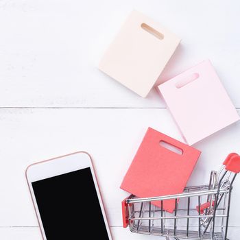 Abstract online shopping, mobile payment concept design element, colorful cart and paper bags on white wooden table background, top view, flat lay