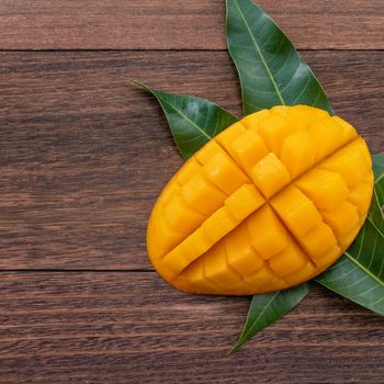 Fresh mango,beautiful chopped fruit with green leaves on dark wooden table background. Tropical fruit design concept. Flat lay. Top view. Copy space