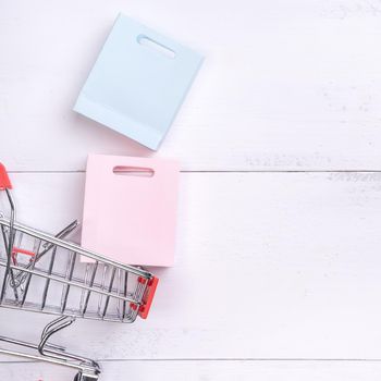 Abstract design element,annual sale,shopping season concept,mini cart with colorful paper bag on white wooden table background,top view,flat lay