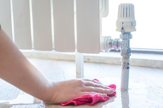 Female hand with rag cleaning water from heating radiator