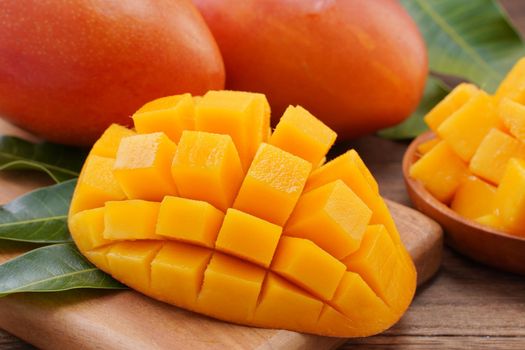 Fresh mango, beautiful chopped fruit with green leaves on dark wooden table background. Tropical fruit design concept. Flat lay. Top view. Copy space