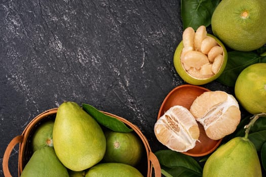 Fresh pomelo, pummelo, grapefruit, shaddock in bamboo basket with leaf on dark black slate background. Seasonal fruit concept. Top view. Flat lay.