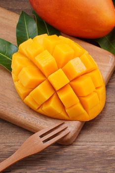 Fresh mango, beautiful chopped fruit with green leaves on dark wooden table background. Tropical fruit design concept. Flat lay. Top view. Copy space