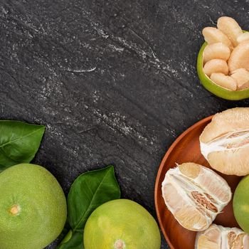 Fresh pomelo, grapefruit in bamboo basket with green leaf on dark black slate background. Seasonal fruit for Mid-Autumn Festival. Top view. Flat lay.