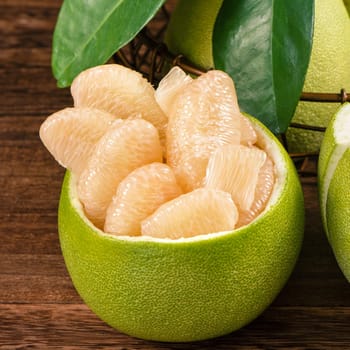 Fresh peeled pomelo, grapefruit, shaddock with green leaves on dark wooden plank table. Seasonal fruit near mid-autumn festival, close up, copy space