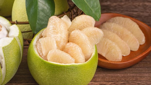 Fresh peeled pomelo, grapefruit, shaddock with green leaves on dark wooden plank table. Seasonal fruit near mid-autumn festival, close up, copy space