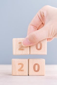 Abstract 2020 & 2019 New year countdown design concept - woman holding wood blocks cubes on wooden table and blue background, close up, copy space.