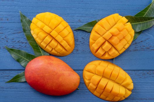 Fresh mango - beautiful chopped fruit with green leaves on dark blue timber background. Tropical fruit design concept. Flat lay. Top view. Copy space