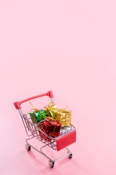 Annual sale, Christmas shopping season concept - mini red shop cart trolley full of gift box isolated on pale pink background, copy space, close up