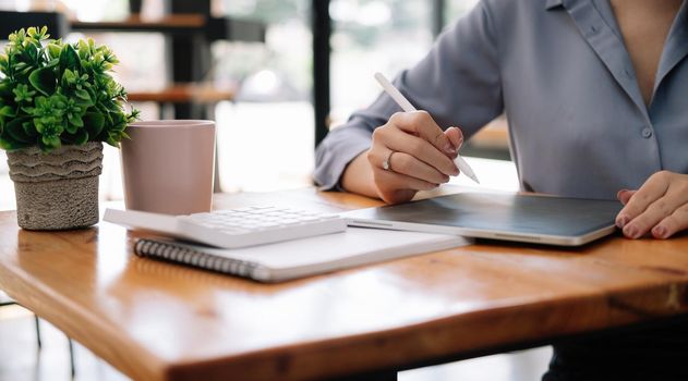 Close up business accountant using digital tablet for calculate finance on wooden desk.