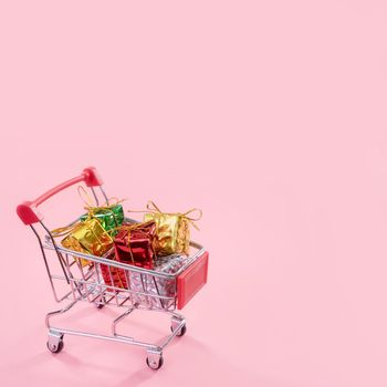 Annual sale, Christmas shopping season concept - mini red shop cart trolley full of gift box isolated on pale pink background, copy space, close up