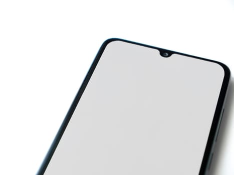 Black mobile smartphone mockup lies on the surface with blank screen isolated on white background. Top view closeup with selective focus and copy space, cut in the middle.