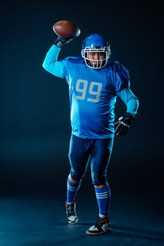 Portrait of a man in a blue uniform for american football throws the ball on a black background