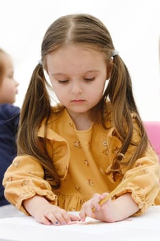 Cute young european kid girl painting with colored pencil. Kindergarten children education concept.