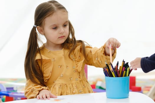 European kid girl painting with colored pencil. Kindergarten children education concept.