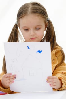 A preschooler girl is looking at a drawing she has drawn.