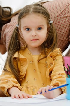 Cute young european kid girl painting with colored pencil. Kindergarten children education concept.