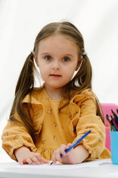 Happy european kid girl draws painting with colored pencil.