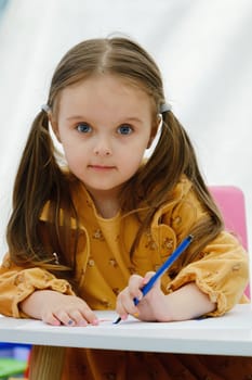 Happy european kid girl draws painting with colored pencil.