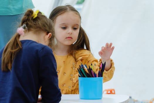 Cute european kid girl painting with colored pencil. Kindergarten children education concept.