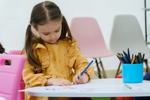 Kid girl painting with colored pencil. Kindergarten children education concept.