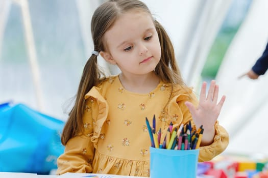 Cute european kid girl painting with colored pencil. Kindergarten children education concept.