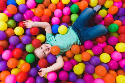 Smiling boy playing lying on colorful balls in the park.