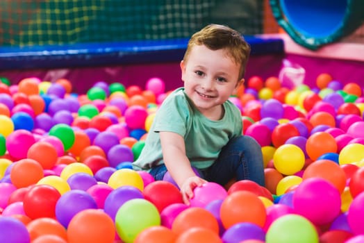 Happy laughing child laughing in an indoor play center. Children playing with colored balls in the playground ball pool. Party.