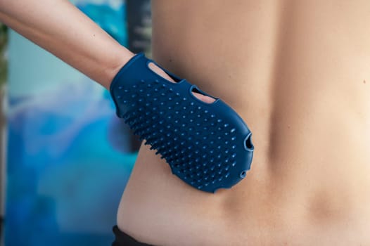 Anticellulite silicone or rubber massager - mitten for body in female hand on body background.