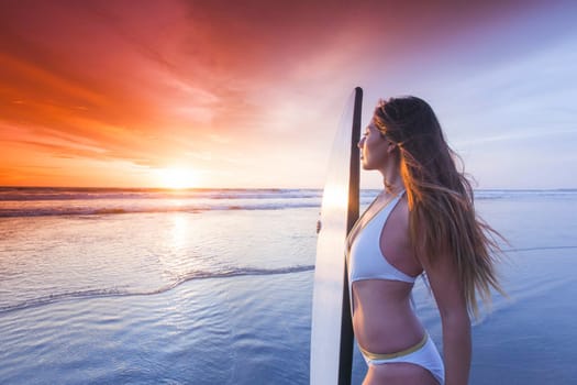 Beautiful surfer woman on the beach at sunset