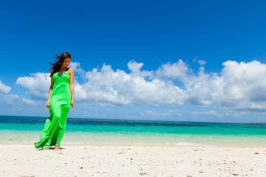 Beautiful young woman in green dress walking on beach