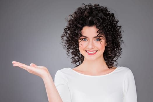 Portrait of amazing beautiful smiling woman with curly hair on gray background showing copy space
