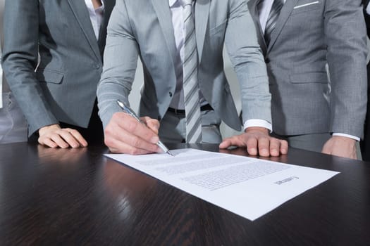 Businessman signing contract while his team is looking at him