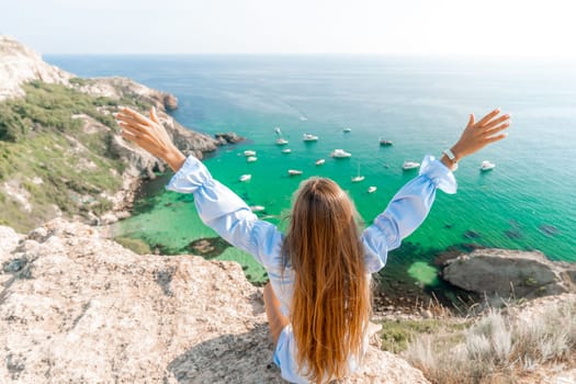 Woman travel sea. Happy woman in a beautiful location poses on a cliff high above the sea, with emerald waters and yachts in the background, while sharing her travel experiences.