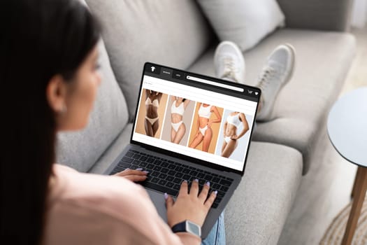 Millennial arabic woman shopaholic enjoy online shopping, buy underwear on laptop screen, sitting on sofa in living room. Website, app for fashion, order delivery, sale at home