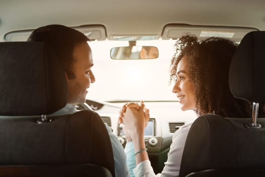 Road Trip. Rear View Of Young Arabic Couple In Car Holding Hands Enjoying First Ride In New Auto, Sitting On Front Driver And Passenger Seats Inside. Joy Of Vehicle Ownership And Family Journey