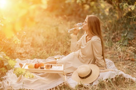 Woman picnic vineyard. Romantic dinner, fruit and wine. Happy woman with a glass of wine at a picnic in the vineyard on sunny day, wine tasting at sunset
